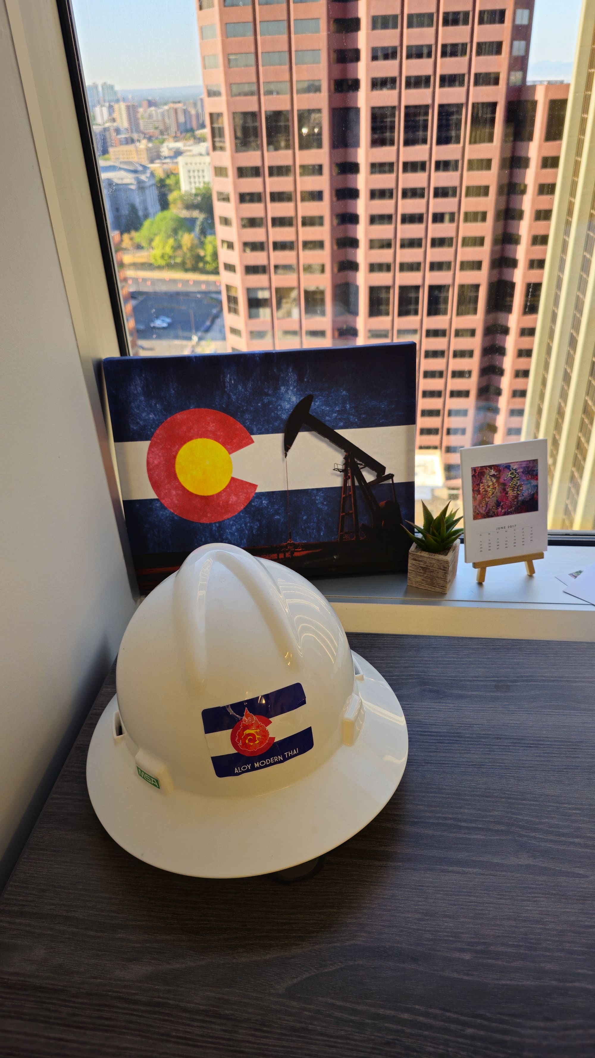 Colorado flag artwork with a pumpjack, beside a Trinity hard hat